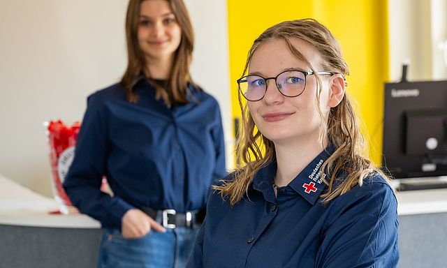 Junge Auszubildende zur Kauffrau im Gesundheitswesen am Empfang des DRK-Kreisverbands, freundlich in die Kamera blickend.