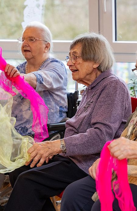 Seniorinnen bewegen pinkfarbene Tücher bei einer Bewegungsrunde