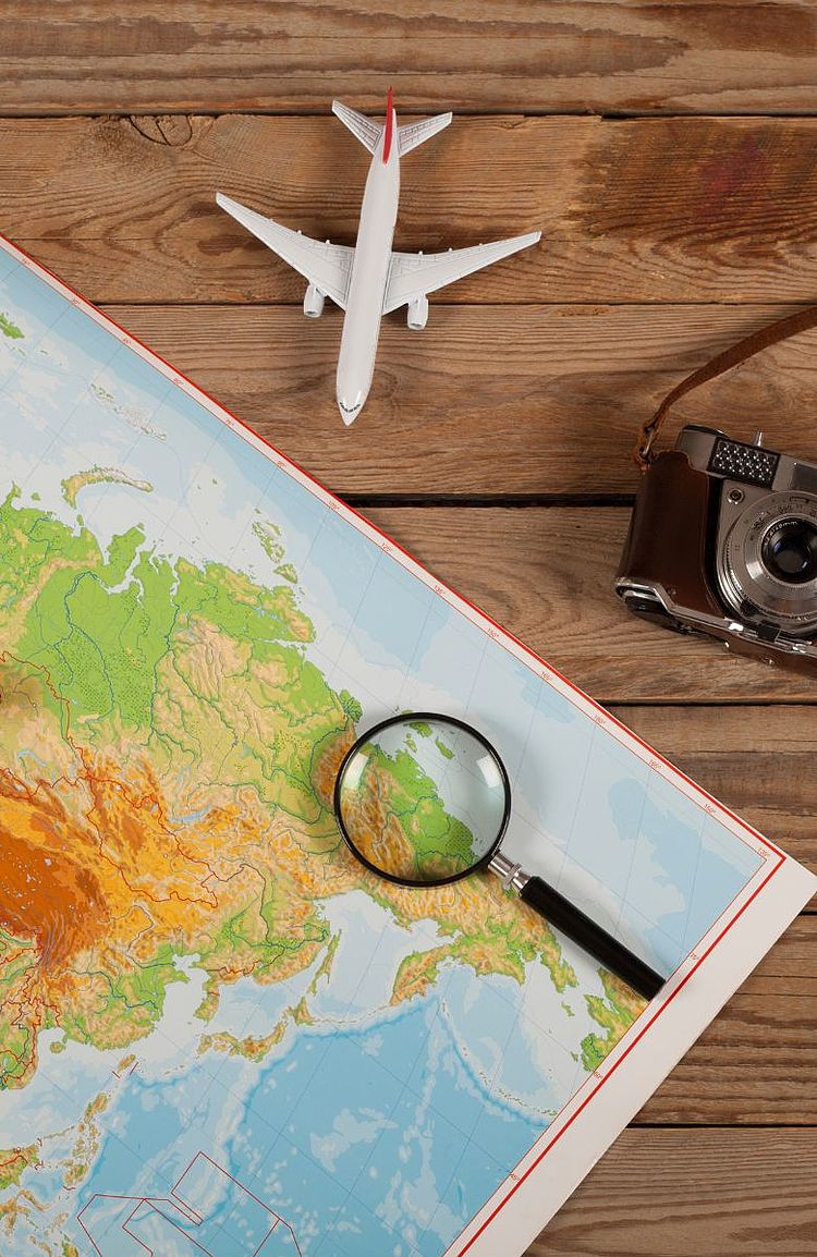 Landkarte mit Lupe, Kamera und Spielzeugflugzeug auf einem Holztisch