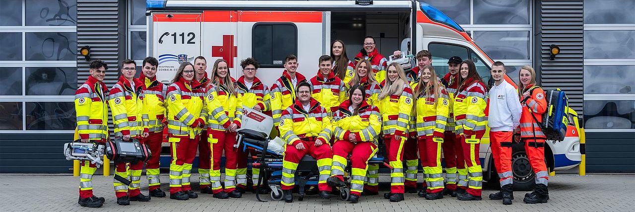 Gruppenfoto der Auszubildenden im Rettungsdienst in Einsatzkleidung vor einem Rettungswagen