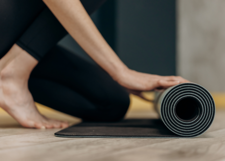 Nahaufnahme einer Person, die eine schwarze Yogamatte auf einem Holzboden ausrollt.
