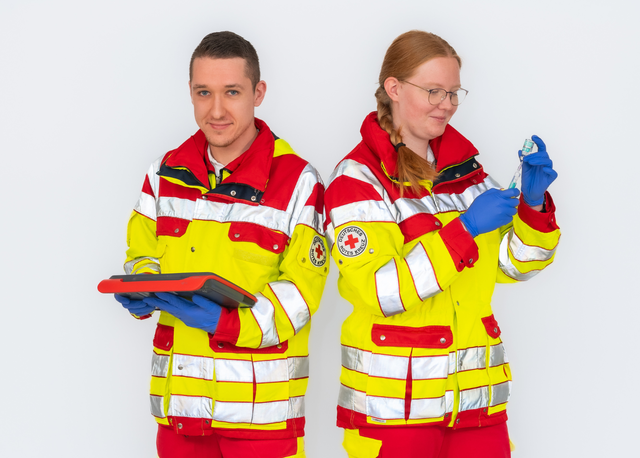 Zwei Mitarbeitende des Rettungsdienstes in Einsatzkleidung, eine Person arbeitet mit einem Tablet, die andere bereitet eine Spritze vor.