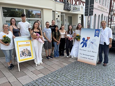 Teilnehmerinnen und Teilnehmer der Babysitting-Ausbildung Sommer 2025 des DRK Schwalm-Eder vor dem M5 Mehrgenerationenhaus in Homberg mit Plakat und Blumen