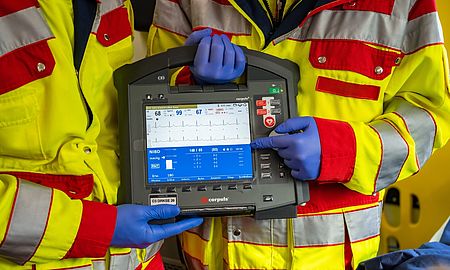 Zwei Einsatzkräfte des DRK Schwalm-Eder in gelb-roter Einsatzkleidung bedienen ein modernes Überwachungsgerät (corpus³) mit EKG-Anzeige und Vitalwerten.