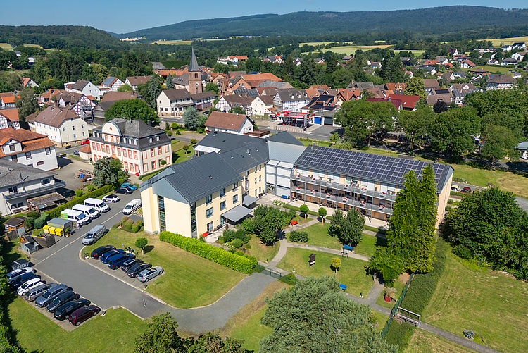 2026-06-15 - Seniorenheim Jesberg_005_klein Luftaufnahme des DRK Seniorenzentrums Kellerwald in Jesberg mit Garten, Terrassen und Solaranlage auf dem Dach, umgeben von der Ortschaft und bewaldeten Hügeln.