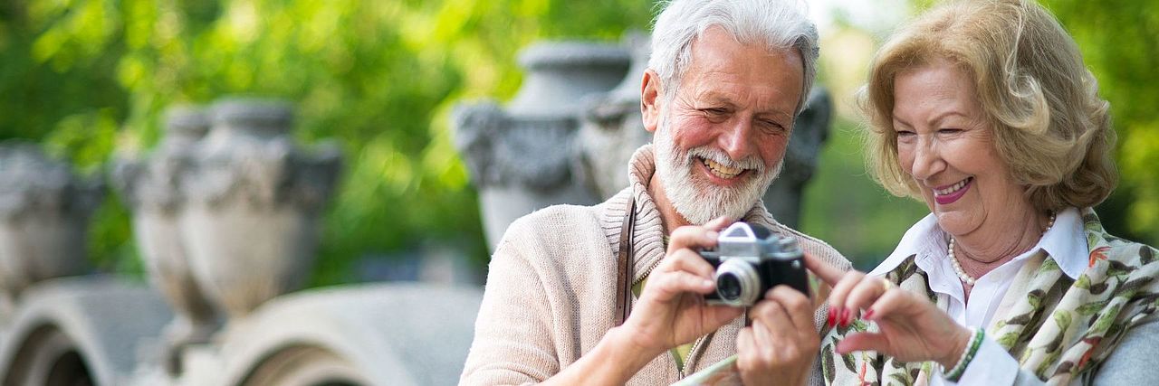 Älteres Paar betrachtet lachend Fotos auf einer Kamera im Freien