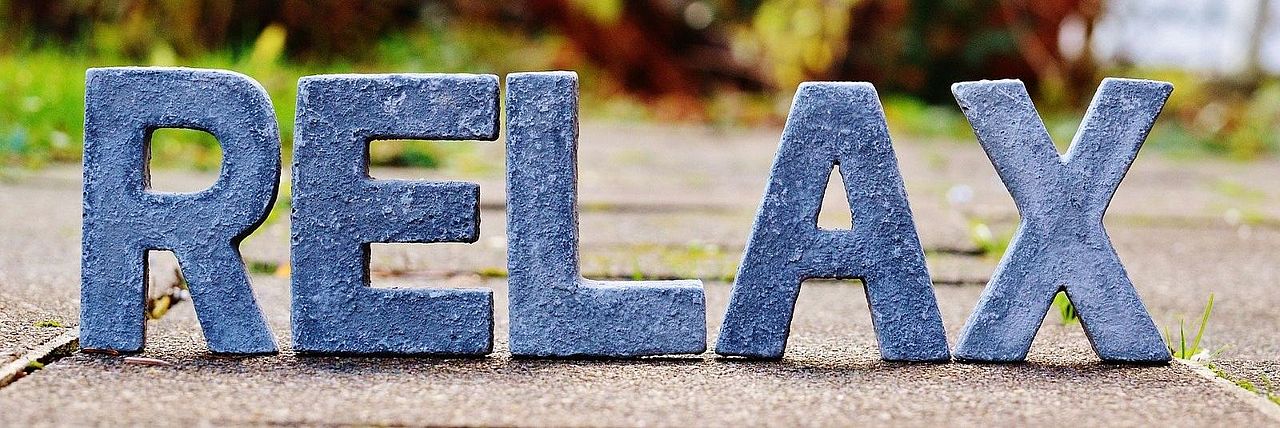 Schriftzug „RELAX" aus blauen Buchstaben vor herbstlichem Hintergrund