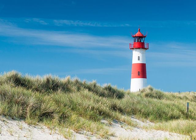 Rot-weißer Leuchtturm hinter Dünen mit Strandgras unter blauem Himmel