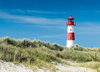 Rot-weißer Leuchtturm hinter Dünen mit Strandgras unter blauem Himmel