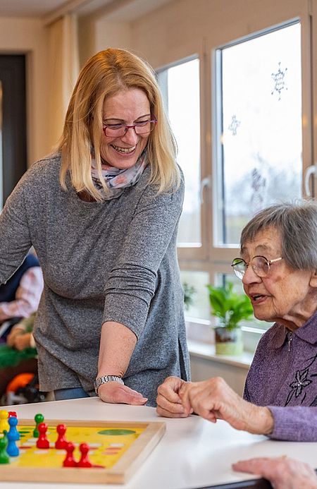 Betreuerin spielt mit einer Seniorin ein Brettspiel am Tisch