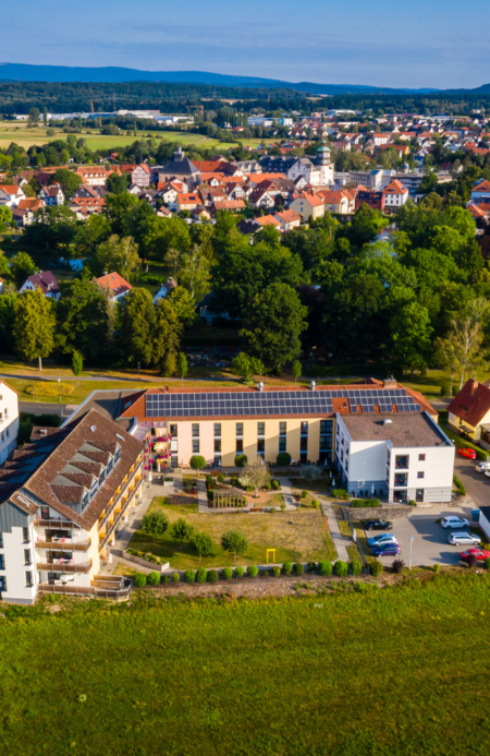 Luftaufnahme der Seniorenresidenz in Schwalmstadt-Ziegenhain mit großer Gartenanlage, Solaranlagen auf dem Dach und Blick auf die umliegende Stadt und Landschaft.