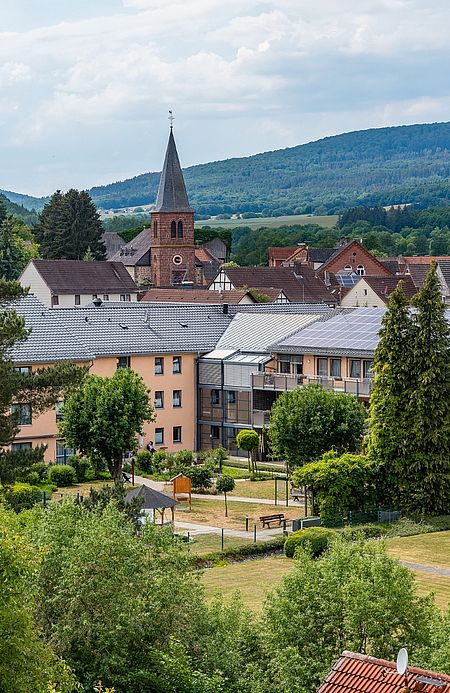 Blick auf die Seniorenresidenz in Jesberg mit Gartenanlage, umgeben von Wohnhäusern und Kirche im Ortskern, im Hintergrund bewaldete Hügel.