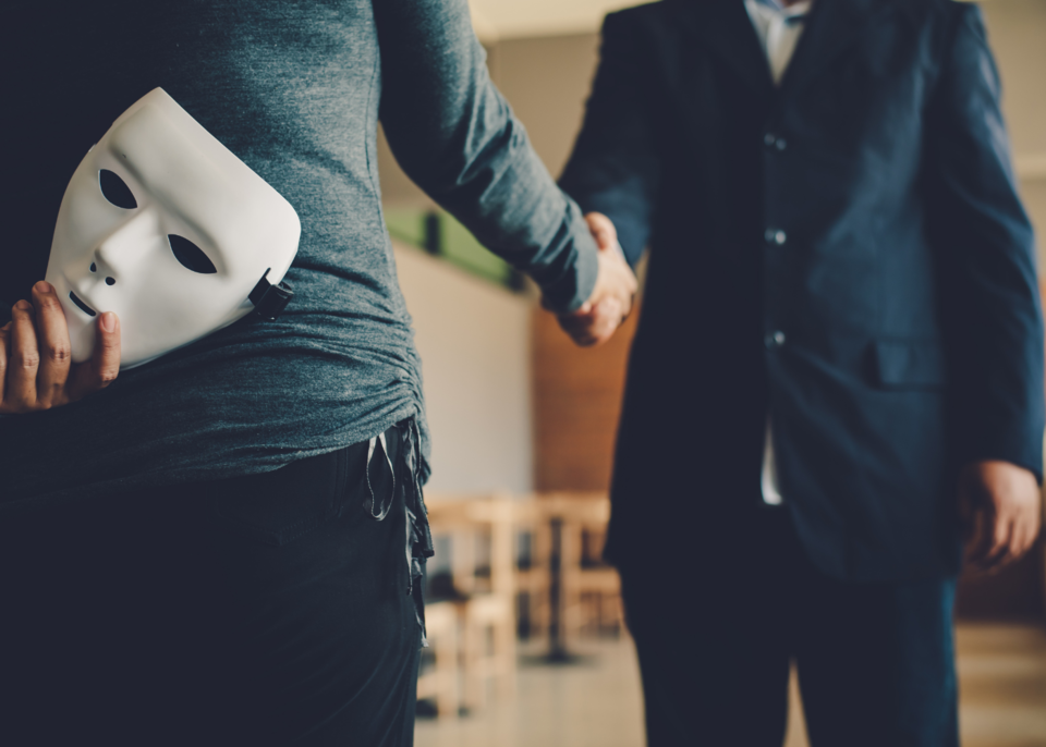 Person mit versteckter Maske gibt jemandem die Hand – Symbolbild für Betrug und Täuschung.