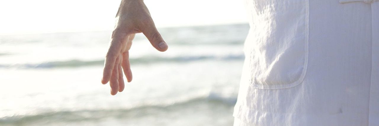 Person in heller Kleidung bei einer Qigong-Bewegung am Meer