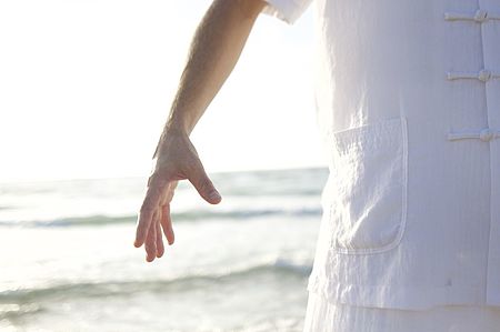Entspannte Person in heller Kleidung am Meer, Arm locker herabhängend, ruhige Bewegung und Atmosphäre von Gelassenheit und Erholung.