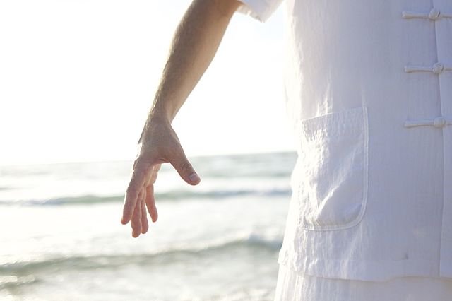 Person in heller Kleidung bei einer Qigong-Bewegung am Meer