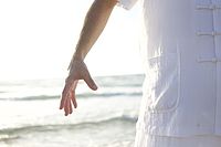 Entspannte Person in heller Kleidung am Meer, Arm locker herabhängend, ruhige Bewegung und Atmosphäre von Gelassenheit und Erholung.