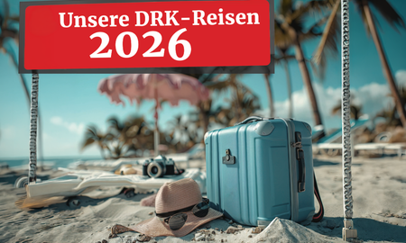 Ein hellblauer Reisekoffer steht im Sand an einem sonnigen Palmenstrand, daneben liegen ein Sonnenhut und eine Kamera. Über der Szene ist ein rotes Banner mit der weißen Aufschrift 'Unsere DRK-Reisen 2026' eingeblendet.