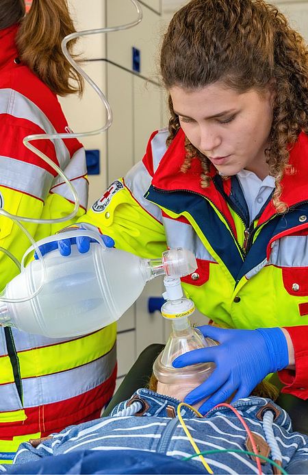 Notfallsanitäterin im Einsatz: Eine junge Frau in roter DRK-Uniform beatmet eine Patientin